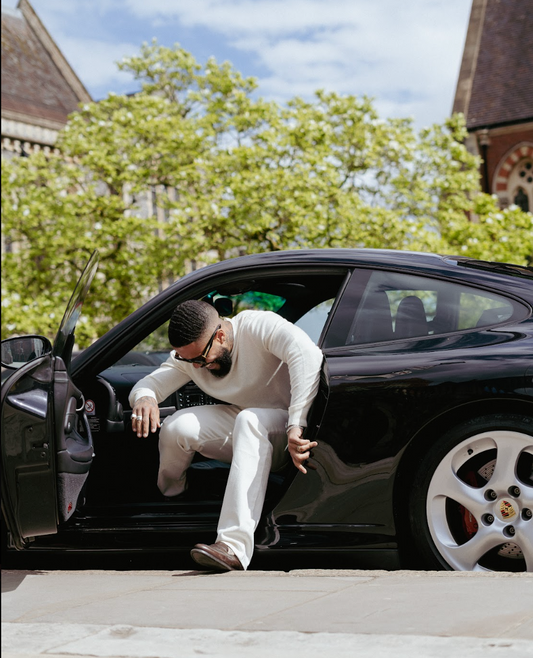 Man in white Vingt Quatre jeans steps out of Porsche 911